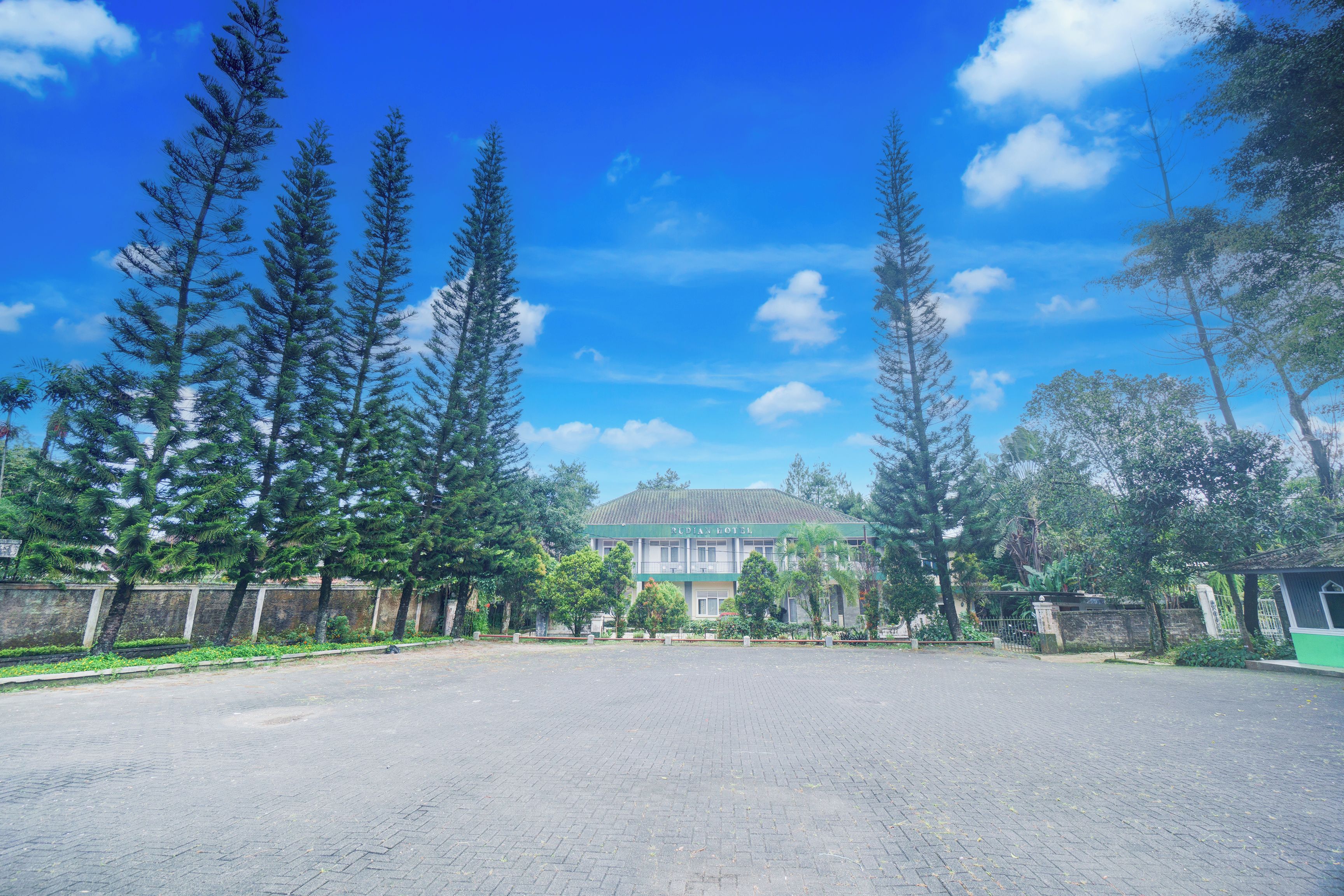 A spacious paved area with tall trees and a building in the background.