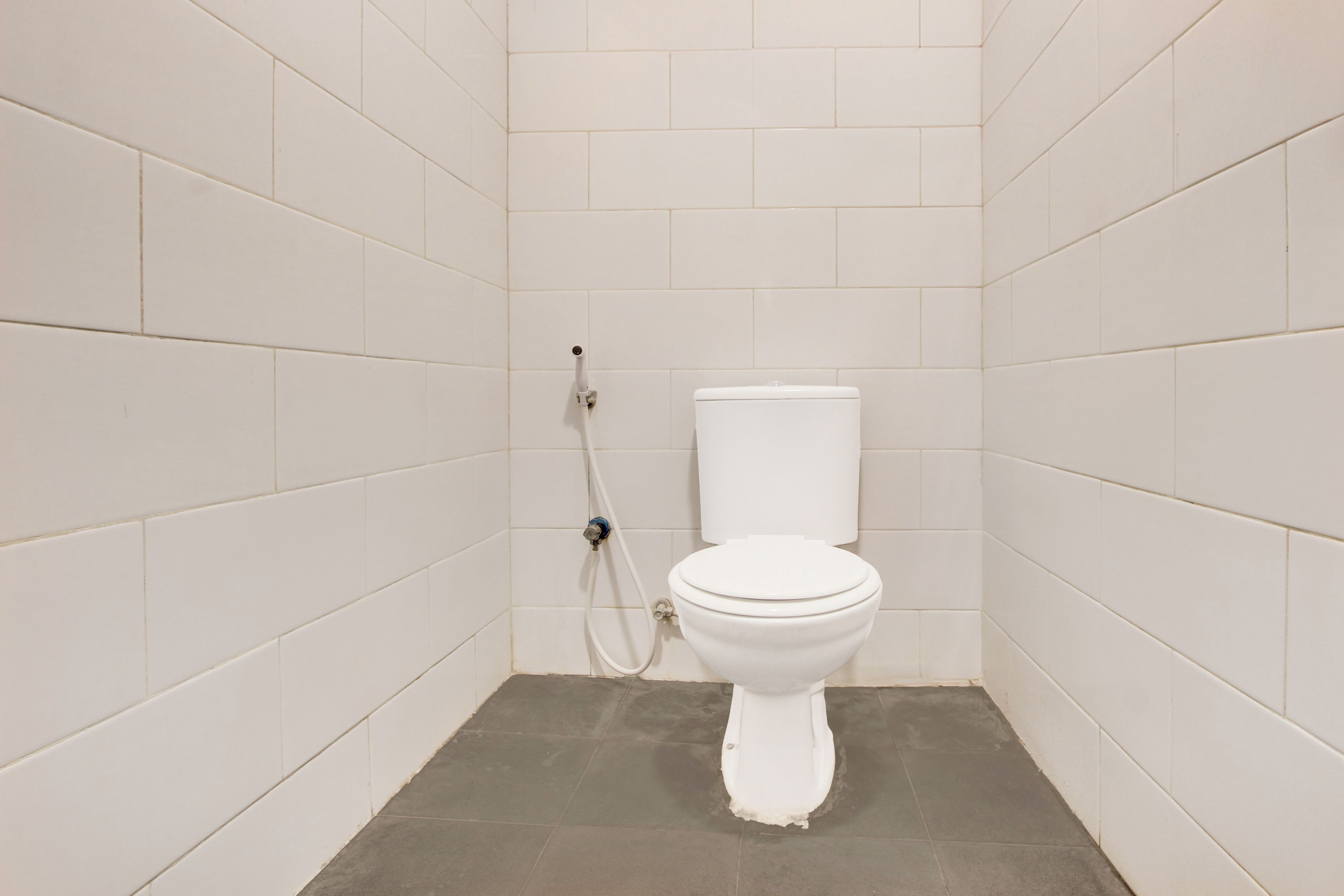 A small, white-tiled bathroom with a toilet and shower.