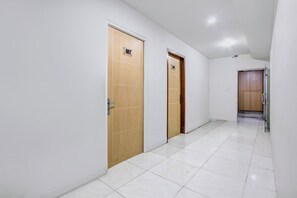A hallway with two wooden doors, white tiled flooring, and a ceiling light. - Hotel O Tegal Near Near Pacific Mall Tegal (Tegal)