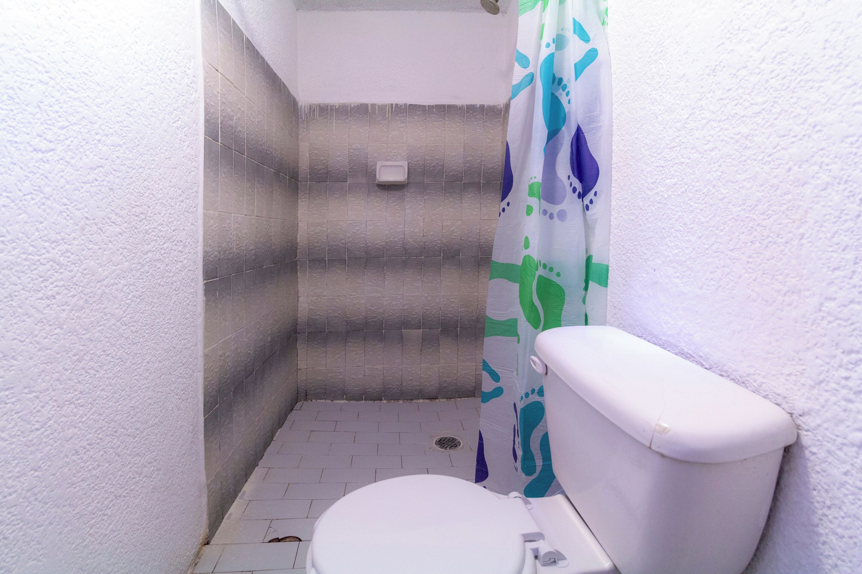 Un baño pequeño con un inodoro blanco, cortina de ducha y suelo de baldosas.
