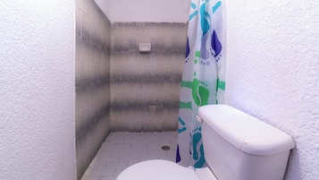Un baño pequeño con un inodoro blanco, cortina de ducha y suelo de baldosas.