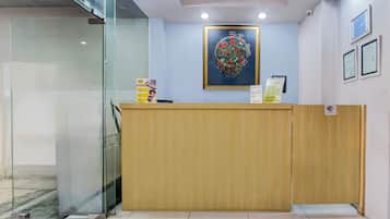 A reception desk with a glass partition, a framed artwork above it, and a signboard on the wall.
