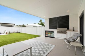 A modern patio with a grill, outdoor seating, and a well-maintained lawn. - The Dunes on Beecroft (Huskisson)