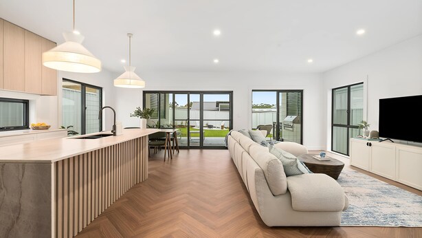 Une cuisine moderne dotée d’un îlot central intégré, un coin repas avec une table et des chaises, un salon avec un canapé et un téléviseur, et de grandes fenêtres offrant une vue sur l’extérieur.