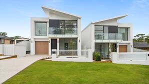 Une maison moderne à deux étages, avec une façade blanche, un porche abrité et une pelouse bien entretenue.