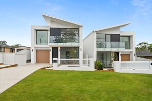 Ein modernes, zweistöckiges Haus mit weißer Fassade, einer überdachten Veranda und einem gepflegten Rasen.