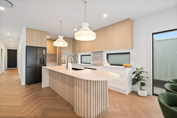 A modern kitchen with a central island, wooden cabinetry, and pendant lighting. - The Dunes on Beecroft (Huskisson)