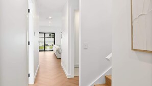Un couloir moderne avec un plancher en bois, des murs blancs et un escalier menant à un autre niveau.