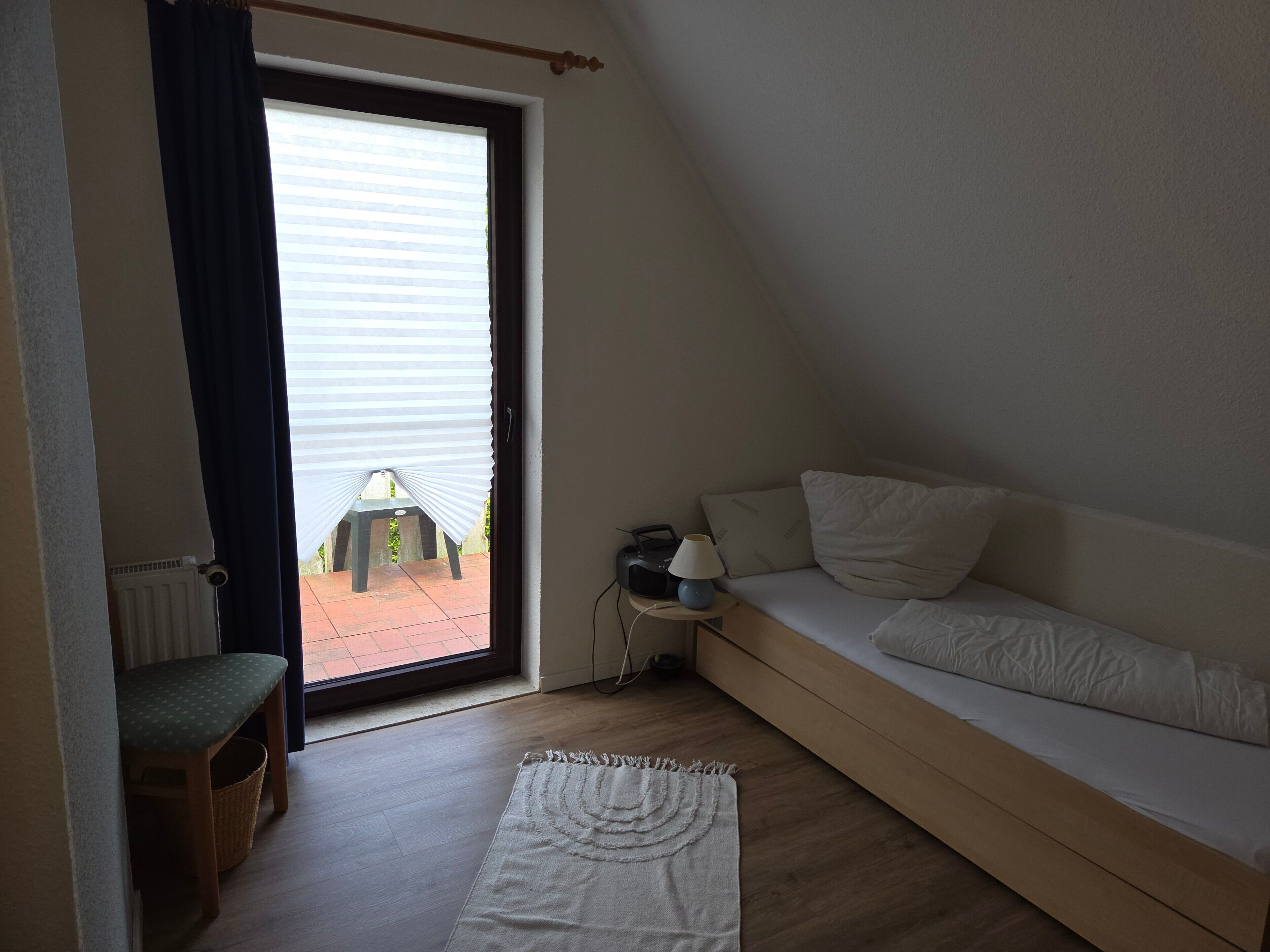A small, cozy room with a single bed, a chair, a table, and a view through a window.