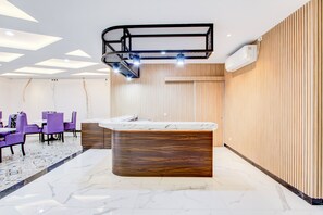 A modern hotel lobby with a reception desk, purple chairs, a marble floor, and a ceiling with geometric light fixtures. - Townhouse Oak Near The Park Mall Semarang (Semarang)