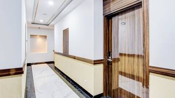 A hallway with a marble floor, a wooden door, and a wall-mounted light fixture.