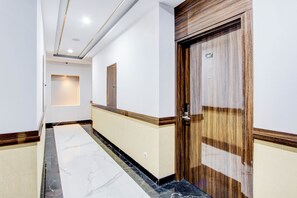 Un pasillo con piso de mármol, una puerta de madera y una lámpara fijada a la pared.