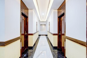 Un pasillo de hotel con piso de mármol, puertas de madera y una lámpara en el centro.