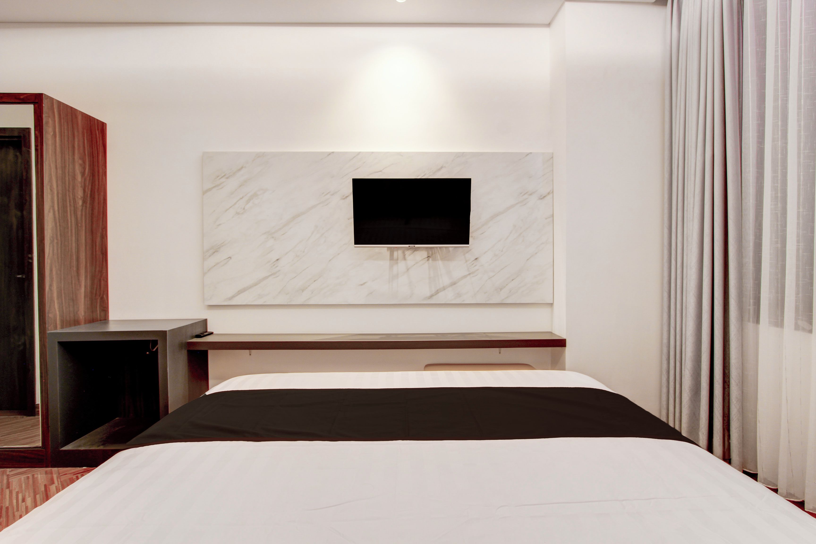 Ett modernt hotellrum med en säng, en platt-TV som är monterad på en vägg av marmor, ett litet skrivbord och en garderob.