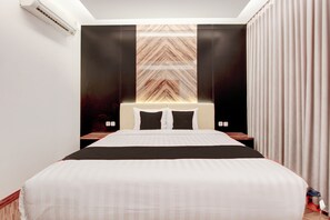 Quarto de hotel com uma cama grande, cabeceira com padrão geométrico, mesa de cabeceira e ar condicionado fixado na parede.