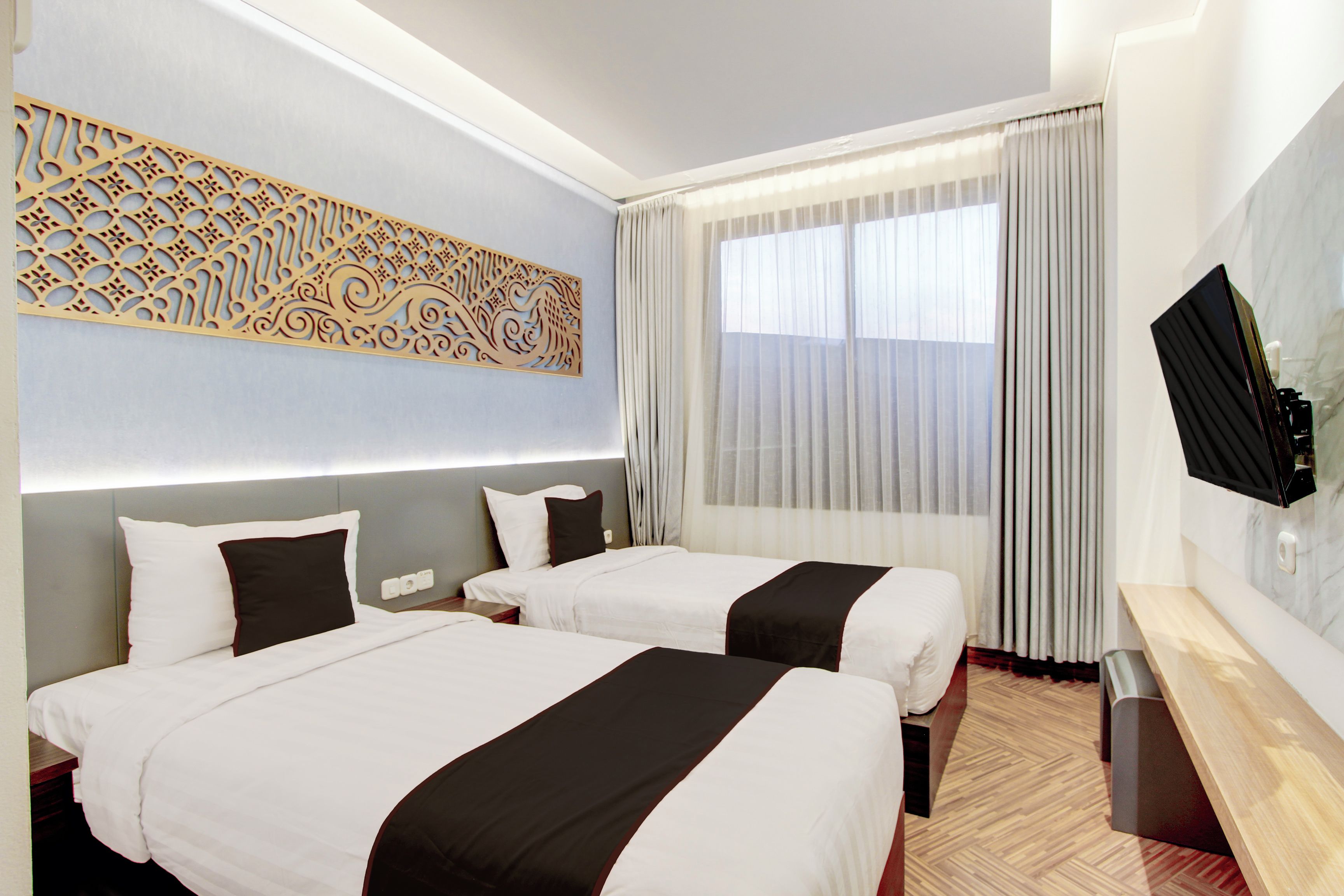 A hotel room with two beds, a TV, a decorative wall piece, and a large window with curtains.