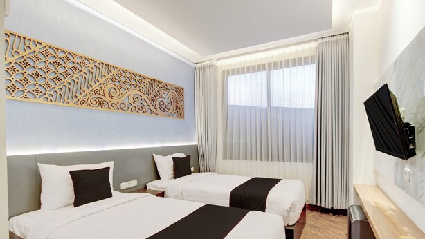 A hotel room with two beds, a TV, a decorative wall piece, and a large window with curtains. - Townhouse Oak Near The Park Mall Semarang (Semarang)