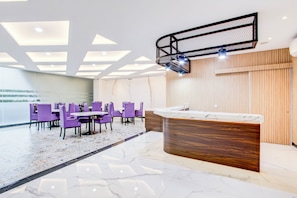 En modern entréhall med en receptionsdisk, lila stolar, ett mönstrat golv och ett tak med infälld belysning.