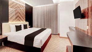 A modern hotel room with a bed, a desk, a TV, and a large window with curtains. - Townhouse Oak Near The Park Mall Semarang (Semarang)