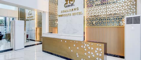 Een hotel receptiebalie met een marmeren aanrecht, een logo en een decoratief houten paneel.