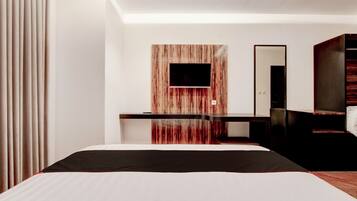 Een moderne hotelkamer met een groot bed, een flatscreen televisie bevestigd aan een wandpaneel van hout, een bureau met stoel, en een spiegel.