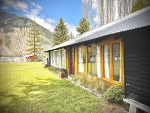 Een chalet met een overdekt terras, een gazon en een berg op de achtergrond.