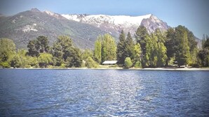 A lake with a mountain in the background and a small building on the shore. - Apartments Bariloche - Moreno Lake (San Carlos de Bariloche)