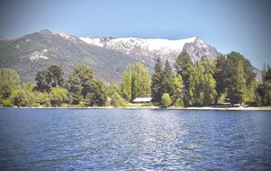A lake with a mountain in the background and a small building on the shore. - Apartments Bariloche - Moreno Lake (San Carlos de Bariloche)