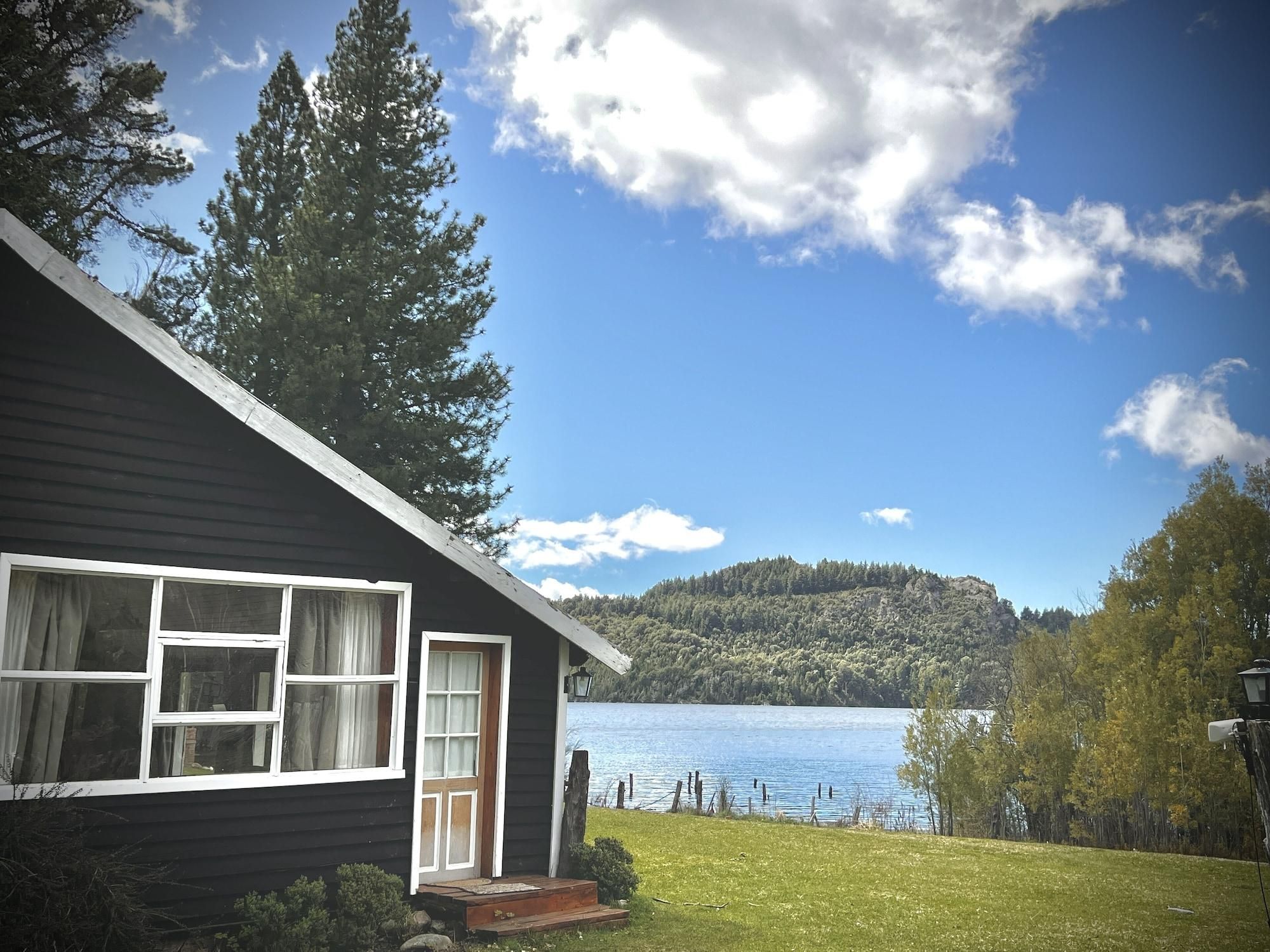 Una cabaña con un ventanal grande, una puerta y vistas a un lago y un bosque.