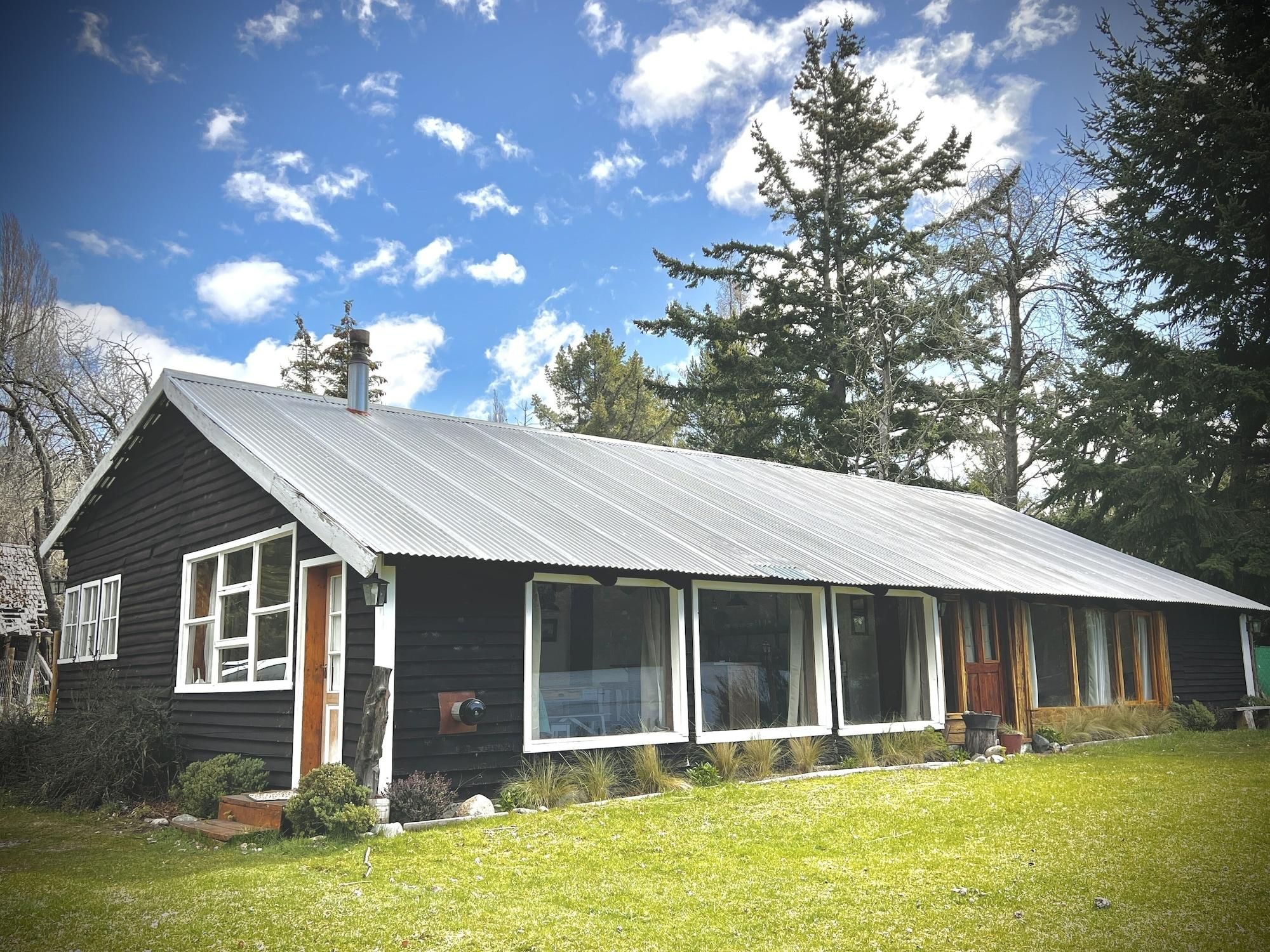 Une cabane rustique avec un toit en métal, de grandes fenêtres et une cour couverte d’herbe.