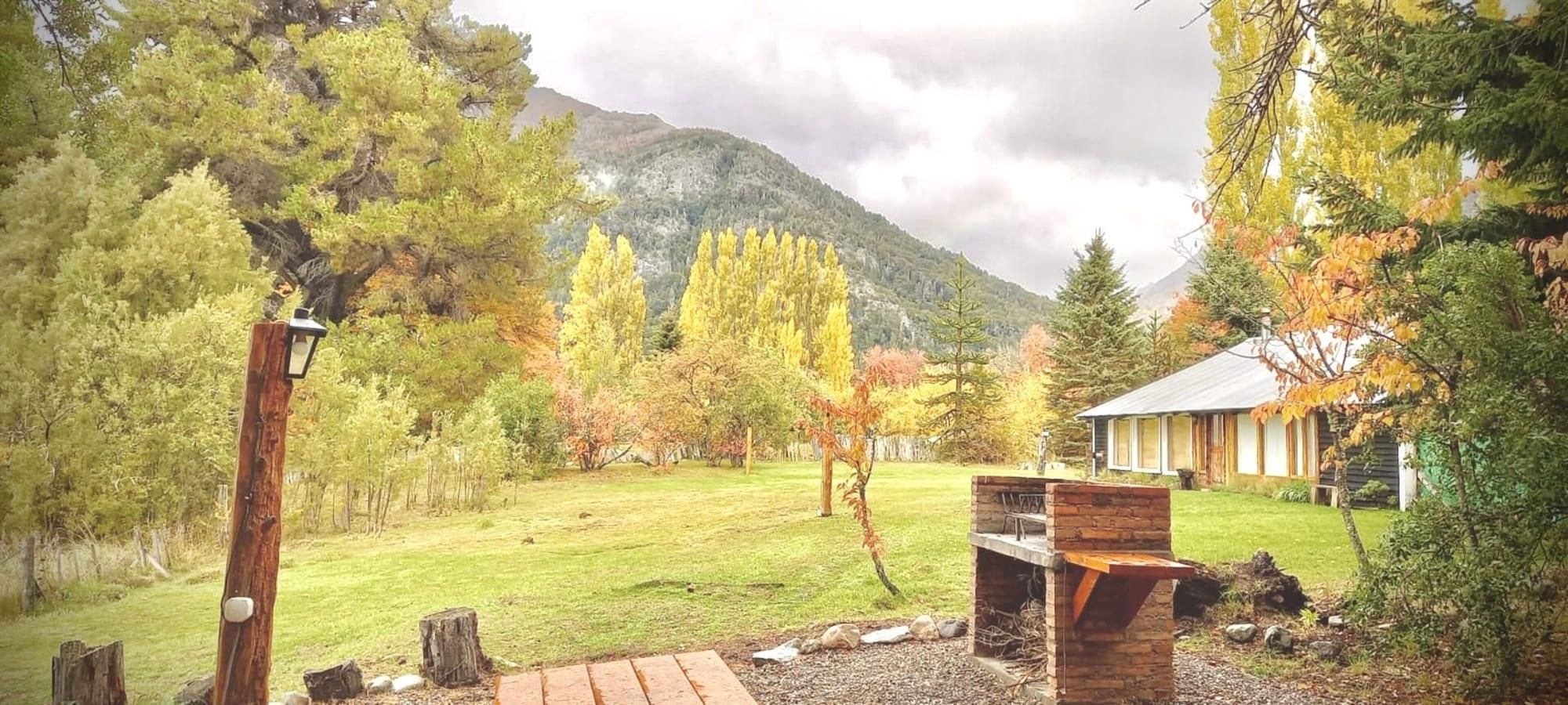 Un espacio exterior rústico con una terraza de madera, una parrilla y una casa al pie de la montaña.