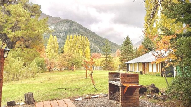 A rustic outdoor area with a wooden deck, a barbecue grill, and a house with a mountain backdrop. - Apartments Bariloche - Moreno Lake (San Carlos de Bariloche)