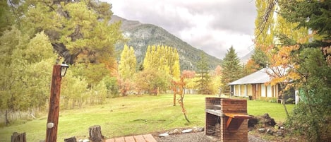 A rustic outdoor area with a wooden deck, a barbecue grill, and a house with a mountain backdrop.