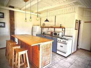Una cocina con una isla de madera, taburetes de bar, estufa, microondas y lámparas colgantes.