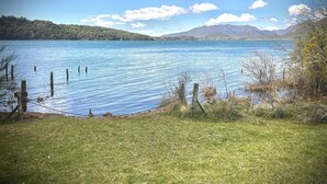 A lake with a grassy shore, wooden posts in the water, and mountains in the background. - Apartments Bariloche - Moreno Lake (San Carlos de Bariloche)