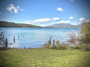 A lake with a grassy shore, wooden posts in the water, and mountains in the background. - Apartments Bariloche - Moreno Lake (San Carlos de Bariloche)