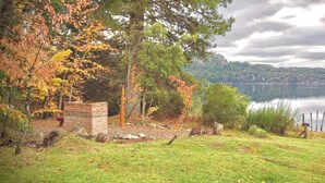 A lakeside view with a grassy area, a stone structure, and a wooden fence. - Apartments Bariloche - Moreno Lake (San Carlos de Bariloche)