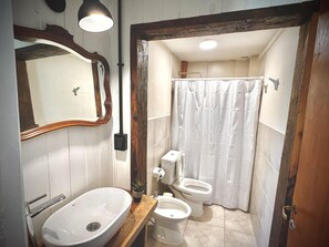 Kylpyhuone, jossa on pesuallas, kaksi wc:tä, suihkuverho ja peili.