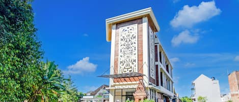 Un edificio con un panel decorativo vertical destacado, una calle empedrada y zonas verdes circundantes.