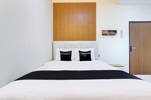 Una cama bien hecha con cabecera blanca y un detalle negro al pie, adornada con dos almohadones decorativos.