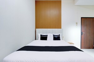 Una cama bien hecha con ropa de cama blanca y negra, un panel de madera en la pared y una puerta de madera.