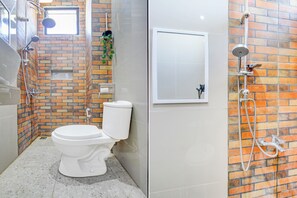 Un baño con inodoro, zona de ducha con manguera y ventana.