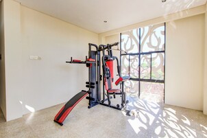 Un gimnasio con equipo de ejercicio, un ventanal con diseños decorativos y suelo de baldosas.