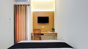 A hotel room with a bed, a desk, a chair, a television, and a curtain. - Collection O Solo Near Univ Muhammadiyah Surakarta (Surakarta)