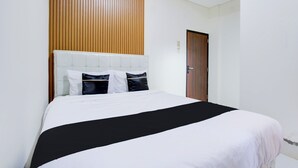 Un lit bien fait, avec une couvre-lit noir et blanc, une tête de lit en bois et deux oreillers.