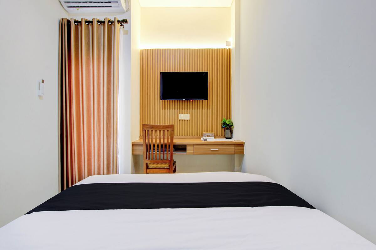 A hotel room with a bed, a desk, a chair, a television, and a curtain.