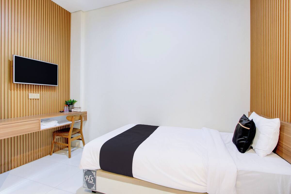 A hotel room with a bed, a desk with a chair, a television, and a small plant.