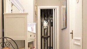 A narrow hallway with a chair, a white shelf unit, and a door at the end. - B B Al Golfo (Salerno)