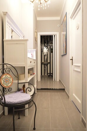 A narrow hallway with a chair, a white shelf unit, and a door at the end. - B B Al Golfo (Salerno)