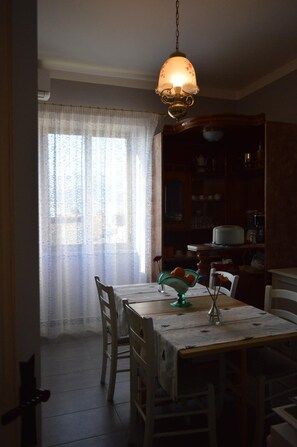 A dining area with a table set for two, a hanging light fixture, and a window with sheer curtains. - B B Al Golfo (Salerno)